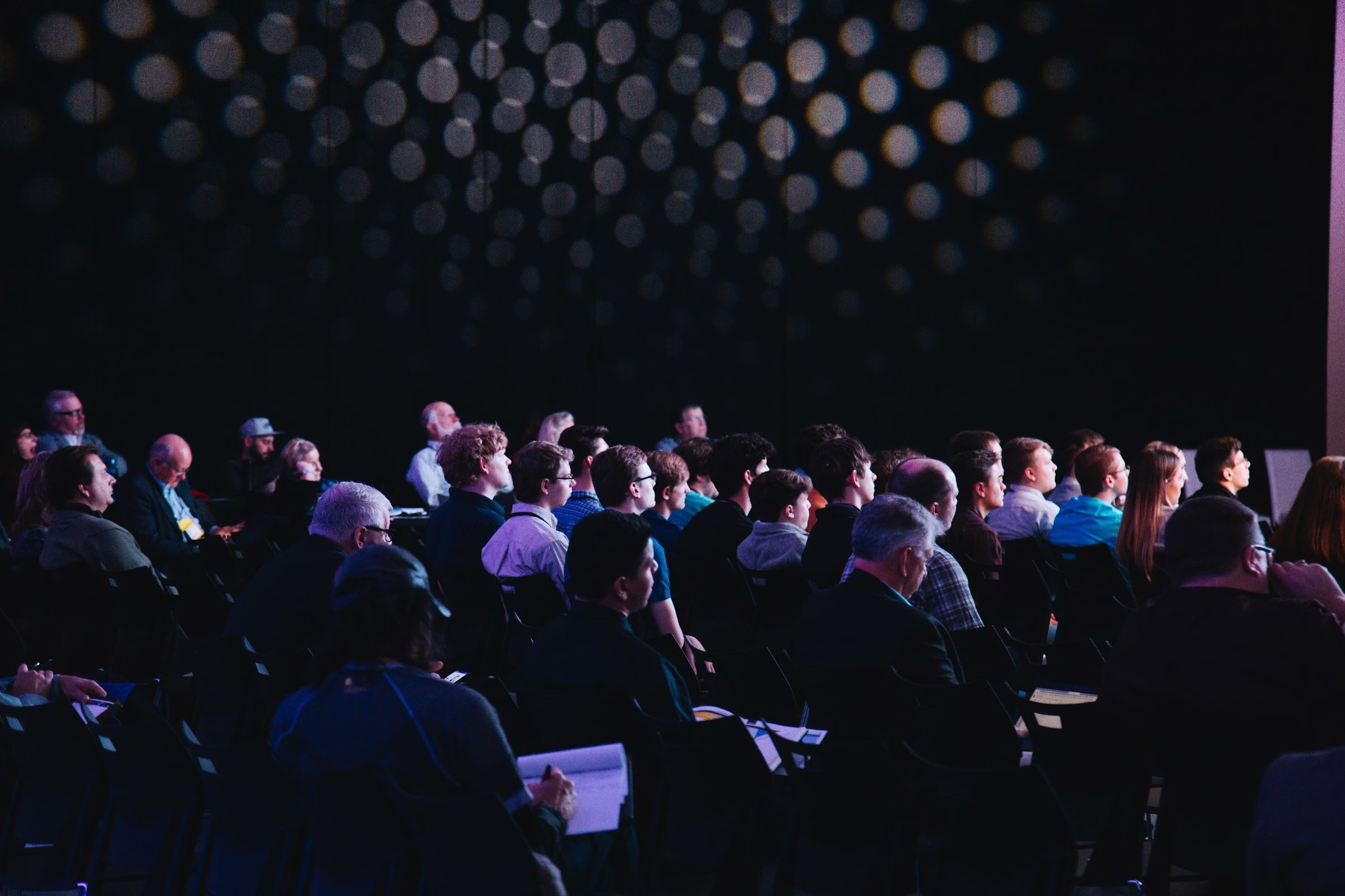 Corporate conference audience seated in professional venue with stage lighting during keynote presentation