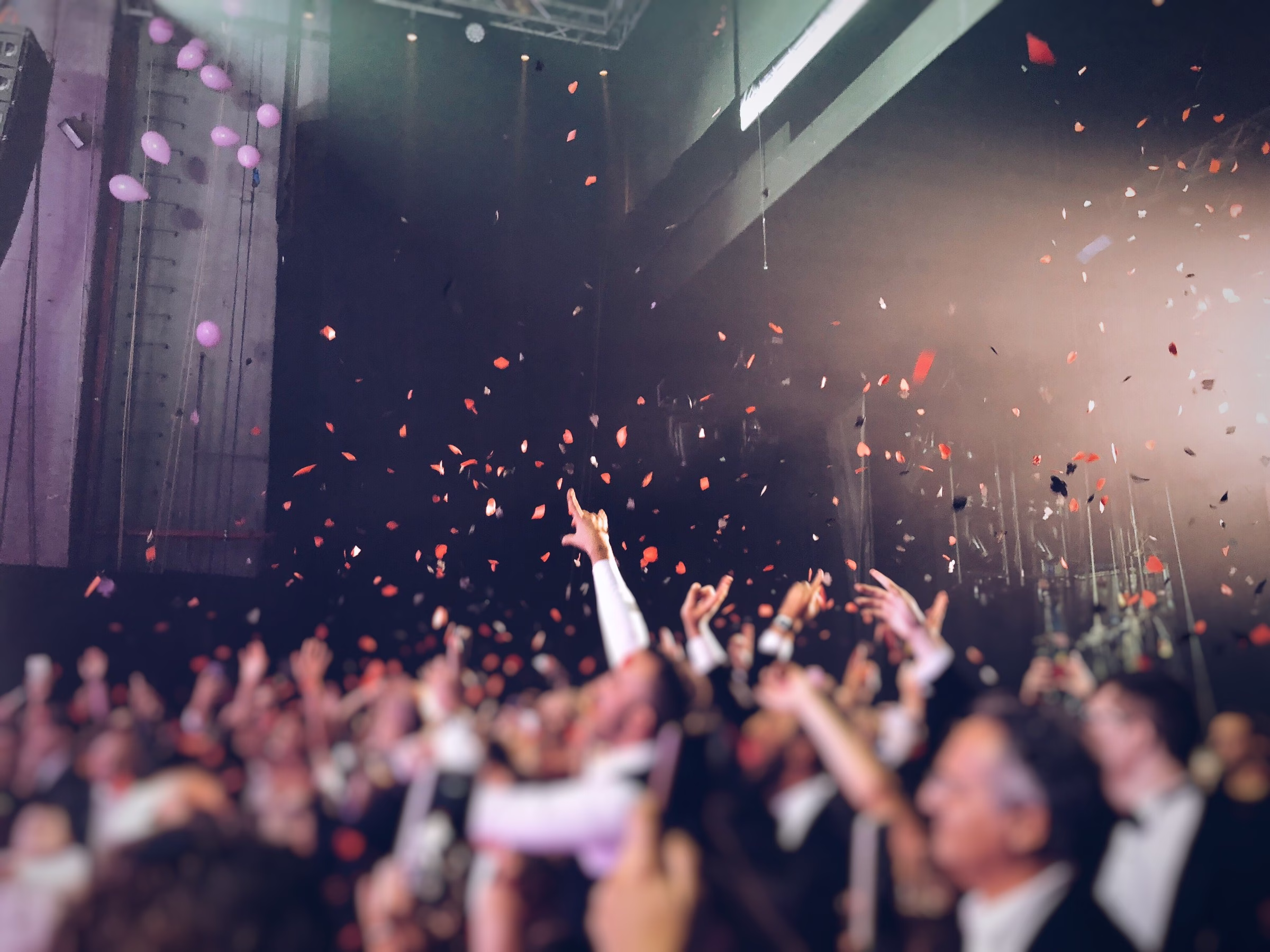 corporate gala confetti drop crowd celebration balloons - Audio/Video Services for Corporate Events in the Triangle Excited crowd with hands raised during a confetti and balloon drop at a corporate gala or awards banquet, with colorful red and pink confetti filling the air above attendees in formal attire inside a large event venue